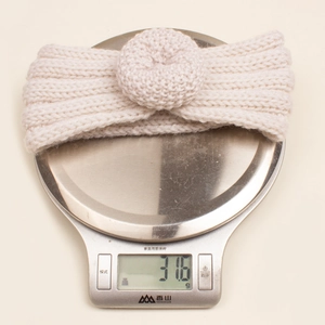 Gros plan détaillé du bandeau tricoté pour bébé beige pesant 31,6 g sur une balance