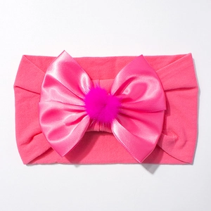 Détail du bandeau en nylon rose pour bébé avec un nœud en satin et un pompon moelleux