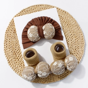 Détail d'un ensemble turban et chaussettes bébé avec nœuds brodés sur fond tissé