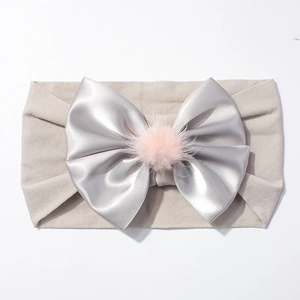Détail d'un bandeau bébé en nylon élastique avec nœud satin gris et pompon rose