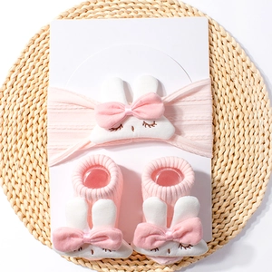 Detail of pink knitted baby headband and socks set featuring cute white rabbit dolls