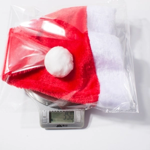 Détail du bonnet de Noël en peluche rouge et blanc emballé pesant 35g sur une balance
