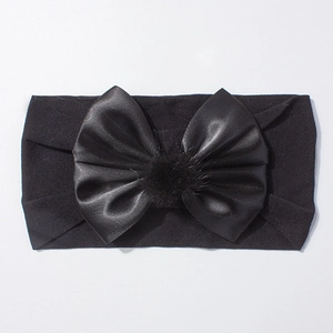 Détail d'un bandeau élastique noir pour bébé avec nœud en satin et pompon en fausse fourrure
