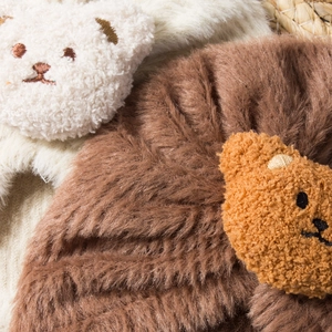 Detailed macro view of soft faux fur texture with cute teddy bear embroidery on warm hats