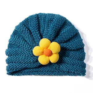 Dettaglio del cappello a turbante in maglia blu scuro con un fiore giallo fatto a mano per neonati
