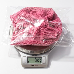 Detail shot of a hot pink knitted baby beanie with a bow, weighing 52.9g on a scale
