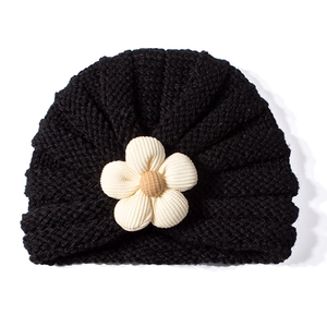 Dettaglio cappello neonato in maglia nera con fiore in velluto crema e perla di legno
