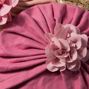 Dettaglio del turbante da neonata rosa con un grande fiore 3D su sfondo di paglia intrecciata
