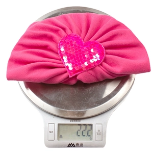Détail d'un turban rose pour bébé avec cœur pailleté pesant 22,2 g sur une balance