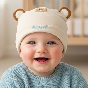 Detail of baby cotton beanie with bear ears and embroidery on beige knit fabric