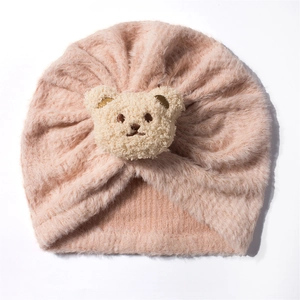 Detail view of a soft pink plush baby hat featuring a cute teddy bear and knotted top