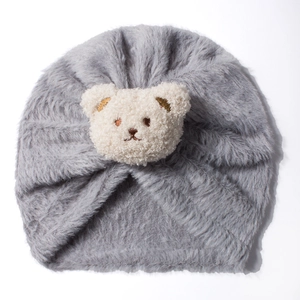 Detail of dark grey plush baby turban hat featuring a cute teddy bear patch on white background