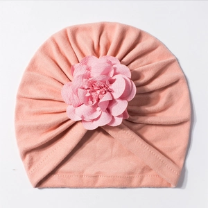 Dettaglio di un cappello a turbante rosa per neonata con grande fiore in tessuto 3D e pieghe