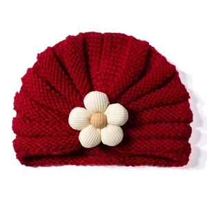 Dettaglio del turbante rosso a maglia per neonati con fiore di velluto bianco e giallo