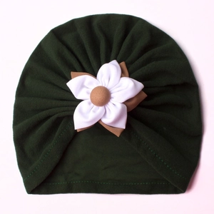 Detail of dark green baby turban hat with a large white cloth flower and pleated design