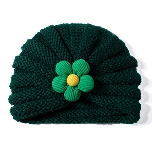 Dettaglio del cappello in maglia verde scuro per neonati con piccolo fiore giallo decorativo