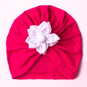 Close-up of baby turban hat in rose red with a large white fabric flower detail