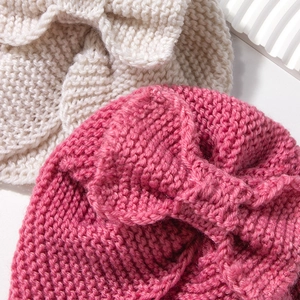 Close-up of knit baby hats with large bows in cream and rose red thick wool texture