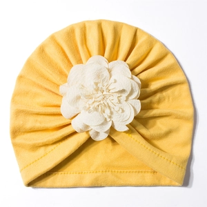 Dettaglio del turbante giallo per neonati con un grande fiore decorativo in tessuto bianco