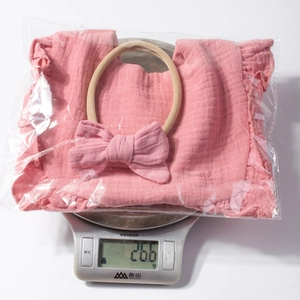 Set bavaglino e fascia per neonata rosa su bilancia che mostra un peso totale di 26,6g