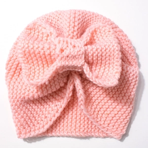 Detail of soft pink knitted baby hat featuring a large decorative knotted bow on top