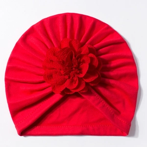 Dettaglio di un cappello a turbante rosso per neonati con grande fiore e trama pieghettata