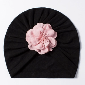 Dettaglio cappello neonato in maglia nera con un fiore rosa in chiffon morbido