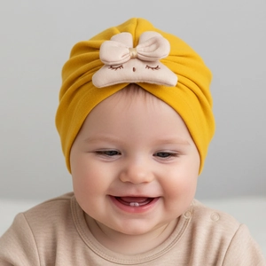 Detail of yellow knit baby turban hat with embroidered smiley face and bow tie decoration
