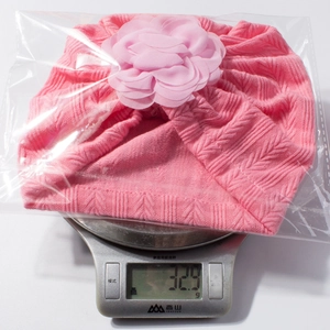 Bonnet en tricot rose pour bébé avec fleur en mousseline pesant 32,9g sur une balance