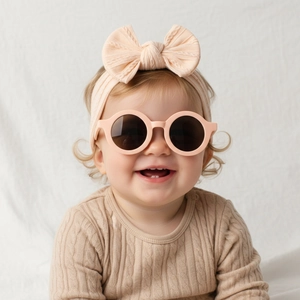 Gros plan d'un bébé avec des lunettes rondes rose mat et un bandeau beige à nœud tricoté