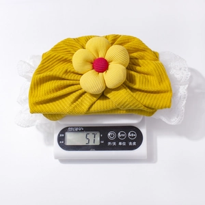 Dettaglio del cappello neonato giallo con fiore che mostra il peso esatto di 57 grammi
