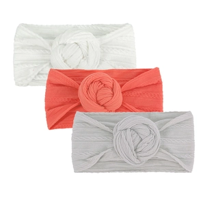 Détail de trois bandeaux bébé en maille torsadée avec nœuds texturés en blanc, rose et gris