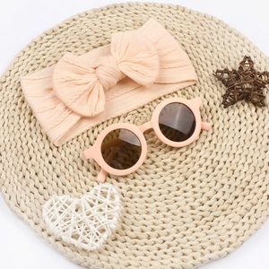 Détail d'un bandeau en maille rose clair avec nœud et lunettes de soleil rondes assorties