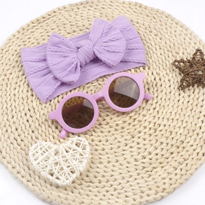 Bandeau à nœud en tricot violet et lunettes de soleil rondes sur un tapis en paille