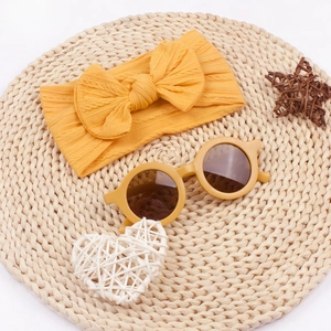 Vue à plat du bandeau à nœud jaune et des lunettes de soleil rondes pour bébé sur un tapis