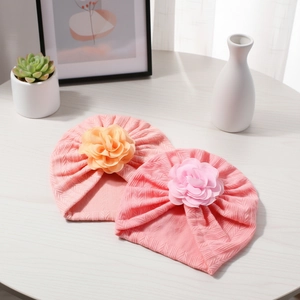 Détail de bonnets turbans pour bébé avec grandes fleurs sur une surface en bois épurée