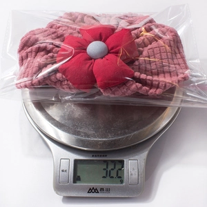 Detail view of pink baby flower beanie showing weight of 32.2g on a scale