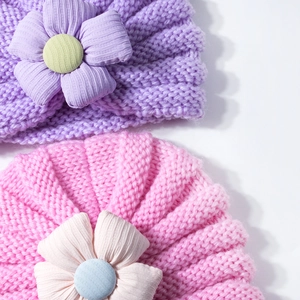 Close-up of knit baby hats featuring large decorative fabric flowers and striped texture