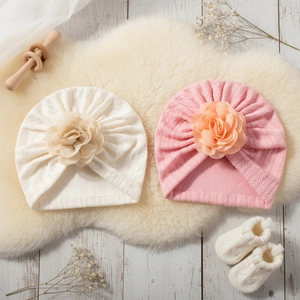 Vue à plat de bonnets tricotés pour bébé en rose et crème avec grandes décorations florales