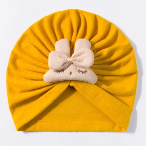 Close-up of yellow baby turban hat featuring pink bow and eyelash embroidery details