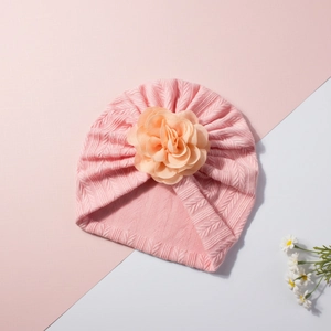 Détail d'un bonnet en tricot rose pour bébé avec une grande fleur et des torsades