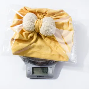 Detailed top view of a yellow baby turban hat with bow, weighing 40 grams on a digital scale