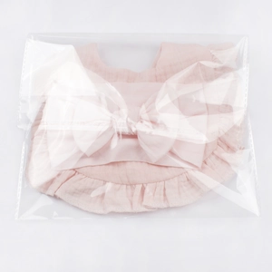 Close-up of pink cotton baby bib set with bow and ruffle details in package