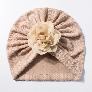 Détail du bonnet turban pour bébé en tricot beige avec une grande décoration florale