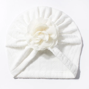 Vue détaillée du bonnet turban blanc pour bébé avec une grande fleur décorative en tissu