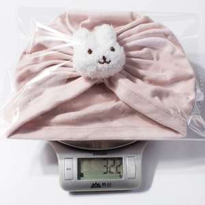 Detailed view of pink knitted baby turban hat with bunny decor on weighing scale