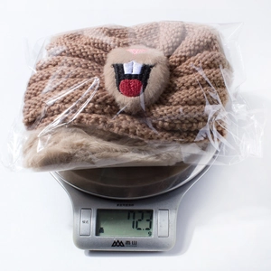 Close-up of brown knit baby hat with plush animal face detail being weighed on a scale