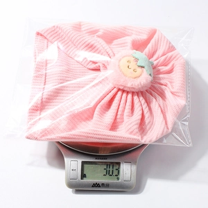 Detailed view of pink waffle knit baby turban with plush strawberry decoration on scales