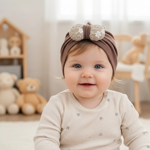 Detailed embroidery of small white flowers on a beige bow of a dark brown baby turban