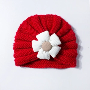 Detail of red knit baby turban hat featuring a white fabric flower and soft texture
